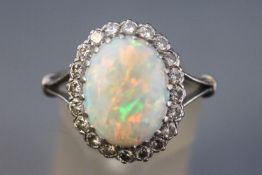 A white metal cluster ring set with an oval cabochon cut opal