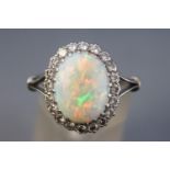 A white metal cluster ring set with an oval cabochon cut opal