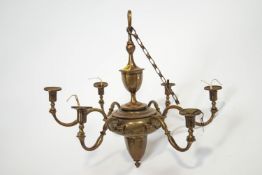 A brass six branch ceiling light suspended from a classical urn over a bulbous motif