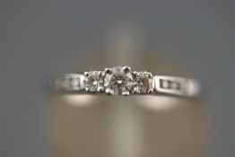 A white metal three stone diamond ring with diamond set shoulders. Hallmarked 9ct gold, Edinburgh.