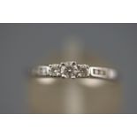 A white metal three stone diamond ring with diamond set shoulders. Hallmarked 9ct gold, Edinburgh.