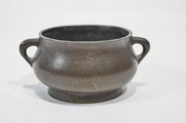 A Chinese bronze two handled pot of small proportions with a plain bellied design, on a wooden base,