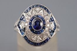 A white metal dress ring principally set with an oval faceted cut blue sapphire