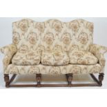 A Jacobean style three seater sofa with domed back over scrolled arms and loose cushions raised on