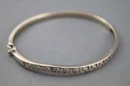 A white metal hinged bangle with cut out Greek key design.