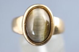 A yellow metal single stone ring set with an oval cabochon cut cats eye chrysoberyl