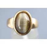 A yellow metal single stone ring set with an oval cabochon cut cats eye chrysoberyl