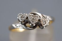 A yellow and white metal ring. Illusion set with three round cut diamonds to heart design settings.