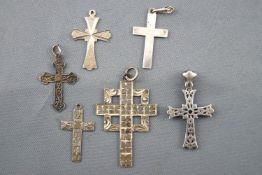 A collection of six white metal cross pendants of variable designs.