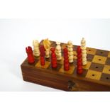 A two tone hardwood travelling chess set in a folding board case,