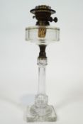 A clear glass and brass oil lamp, with panel cut round reservoir over a similar baluster column,
