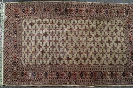 A Bokhara rug, with repeating geometric motifs on a beige ground, within multiple borders,