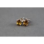 A white metal single stone pair of stud earrings each set with an oval faceted cut orange