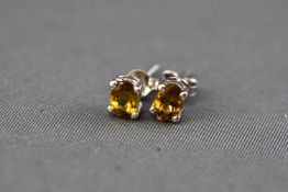 A white metal single stone pair of stud earrings each set with an oval faceted cut orange