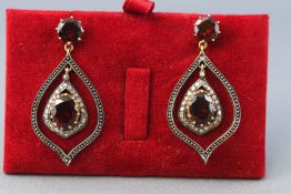 A yellow and white metal pair of drop earrings each set with faceted cut garnets and round cut