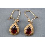 A yellow metal pair of drop earrings each set with a pear cut garnet and finished with a rope