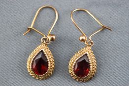 A yellow metal pair of drop earrings each set with a pear cut garnet and finished with a rope