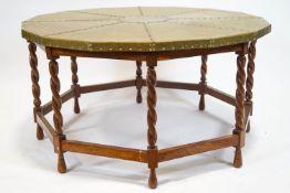 A coffee table with a brass hexadecagon top on an oak frame with barley twist legs linked by