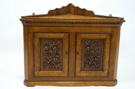 An oak aesthetic movement hanging corner cupboard with crenellated top set over two panel doors,