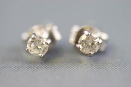 A white metal pair of single stone stud earrings each set with a round brilliant cut diamond