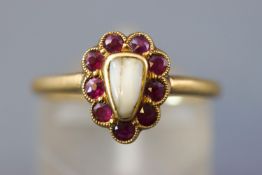 A yellow metal memorial ring set with a halo of rubies surrounding a human tooth.