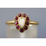 A yellow metal memorial ring set with a halo of rubies surrounding a human tooth.