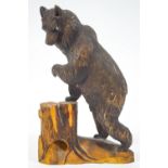 A Black Forest carved wood figure of a bear on his hind legs, resting one paw on a stump, 26.