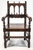 A 17th century oak elbow chair, with open arched back, acorn finials,