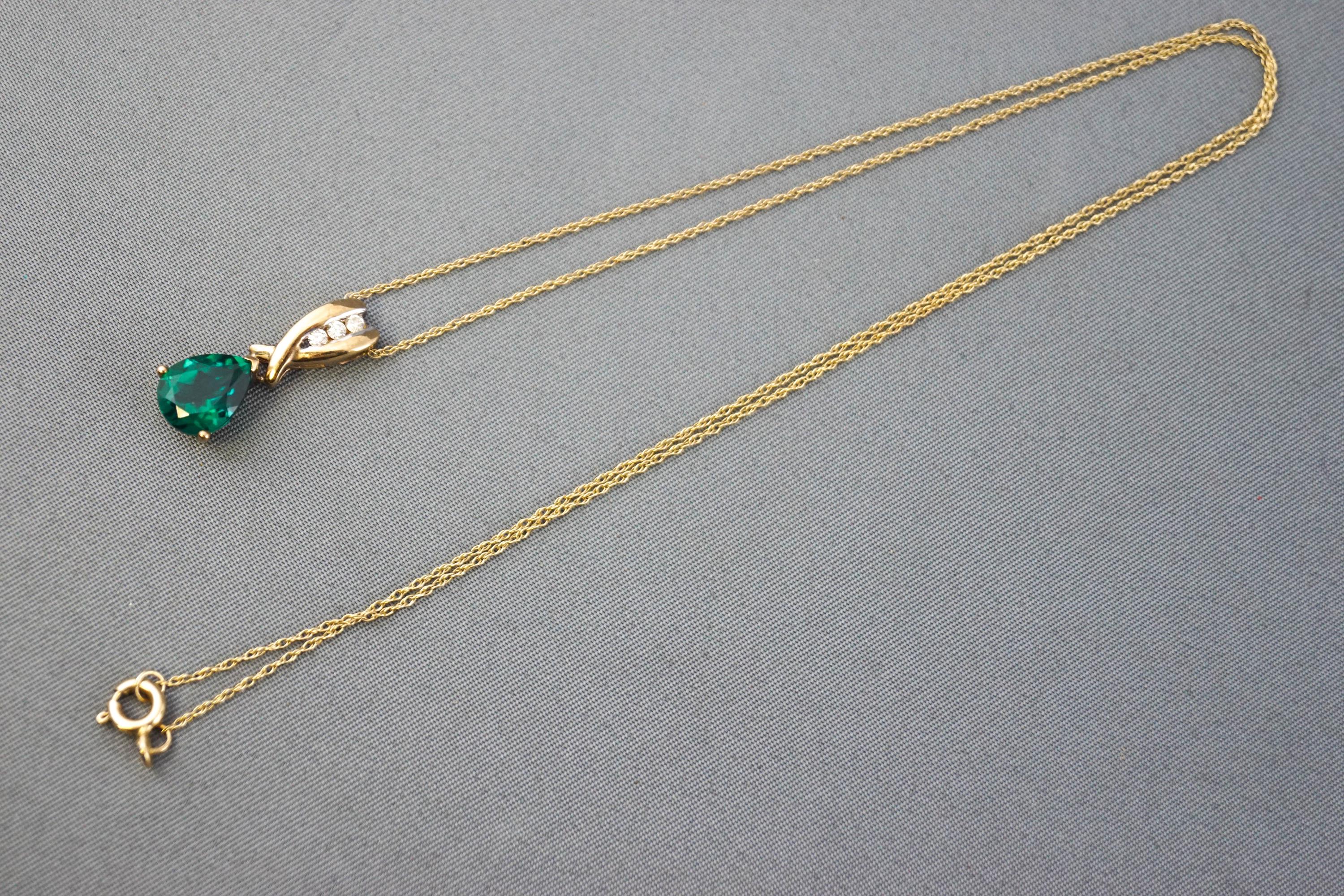 A yellow metal created (synthetic) emerald and diamond pendant suspended from a fine trace link