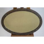 An oval metal framed bevelled wall mirror, decorated with harebell motifs and V emblems,