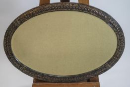 An oval metal framed bevelled wall mirror, decorated with harebell motifs and V emblems,