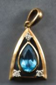 A yellow metal pendant centrally set with a pear cut blue topaz and finished with three round