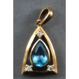 A yellow metal pendant centrally set with a pear cut blue topaz and finished with three round