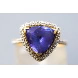 A yellow and white metal cluster ring centrally set with a trilliant cut tanzanite measuring