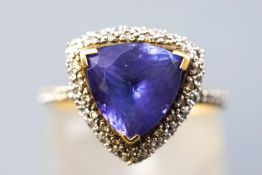 A yellow and white metal cluster ring centrally set with a trilliant cut tanzanite measuring