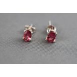 A white metal pair of single stone stud earrings. Each set with a oval faceted cut pink tourmaline.