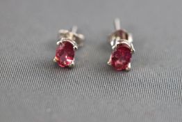 A white metal pair of single stone stud earrings. Each set with a oval faceted cut pink tourmaline.
