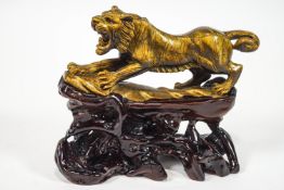 A carved hardstone tiger's eye figure of a snarling lion on a carved root wood stand,