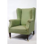 A wing back armchair upholstered in green on square tapering mahogany legs with brass casters,
