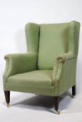 A wing back armchair upholstered in green on square tapering mahogany legs with brass casters,