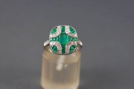 A white metal cluster ring set with a central square faceted cut emerald measuring approximately 5.