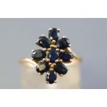 A yellow metal cluster ring set with nine oval faceted cut commercial quality dark blue sapphires.