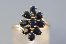 A yellow metal cluster ring set with nine oval faceted cut commercial quality dark blue sapphires.