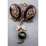 A white metal antique brooch stylized as two oval garnets each embellished with open work leaf