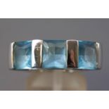 A rhodium plated three stone ring by Swarovski. Set with three square faceted cut blue crystals.