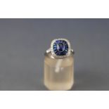 A white metal cluster ring set with a central oval faceted cut sapphire measuring approximately 5.