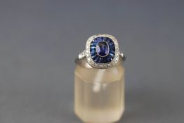 A white metal cluster ring set with a central oval faceted cut sapphire measuring approximately 5.