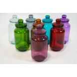 A collection of eight, coloured glass sweet jars and covers, each tinted in different colours,