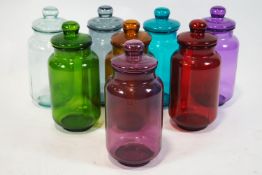 A collection of eight, coloured glass sweet jars and covers, each tinted in different colours,