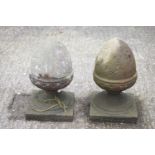 A pair of composite stone acorn finials, raised on a socle on a square plinth,